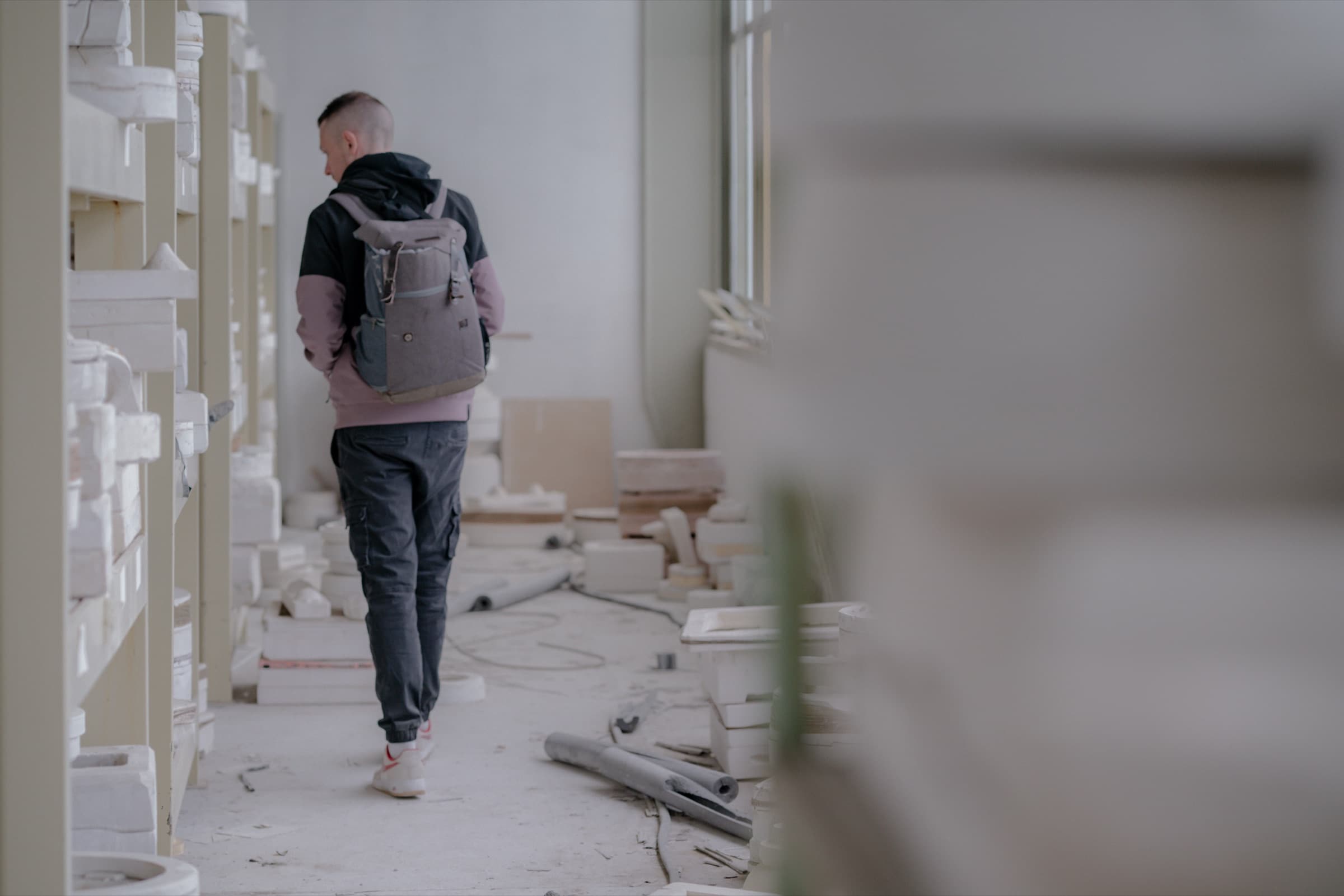 Daniel Boberg läuft mit Rucksack zwischen Regalen voller alter Gipsformen in einer verlassenen Fabrik