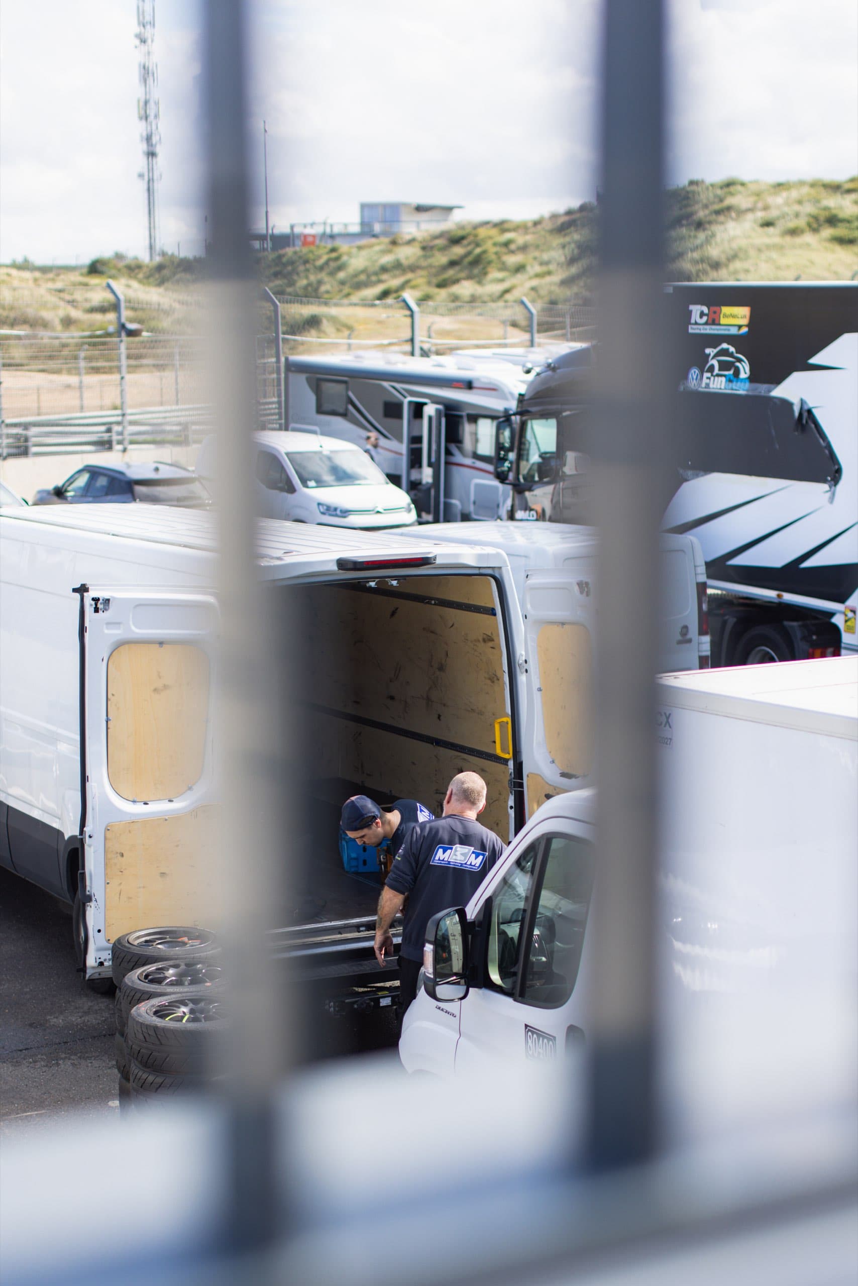 Blick durch einen Zaun auf Transporter im Fahrerlager