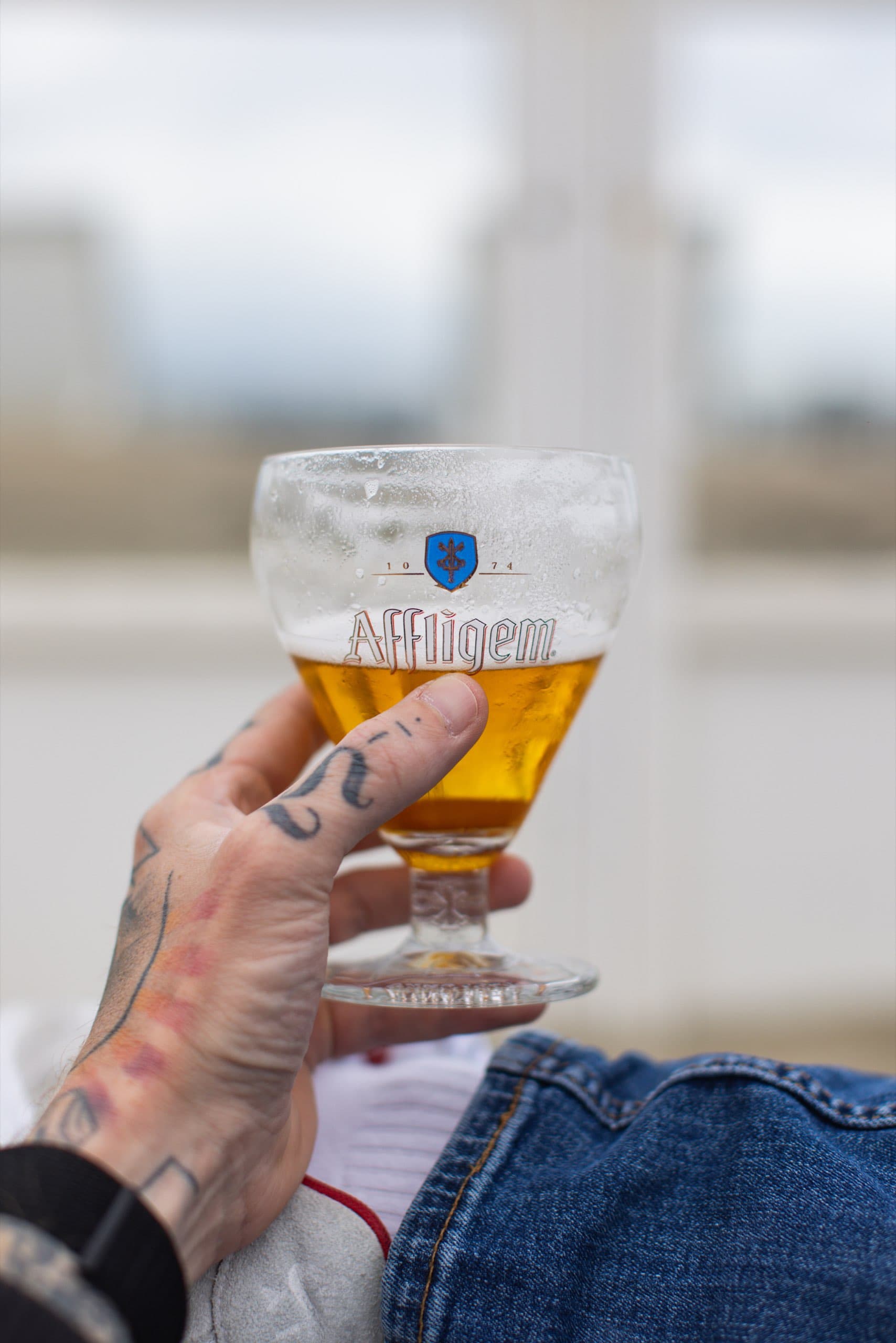 Tätowierte Hand hält ein Glas Bier am Strand
